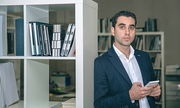 istock Businessman holding smartphone leaning on a bookcase 505912564