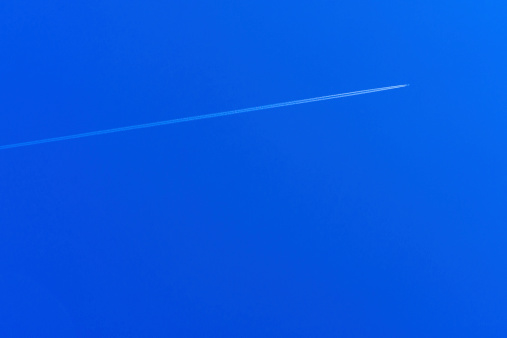 A plane flying through the sky at a diagonal direction with jets trails behind