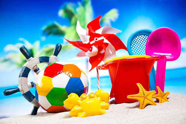 Children's plastic toys green end yellow car, shovel, red bucket, green ball with yellow sand on the beach by sea. Children's beach toys on sand on a sunny day. Sandbox on the playground for games