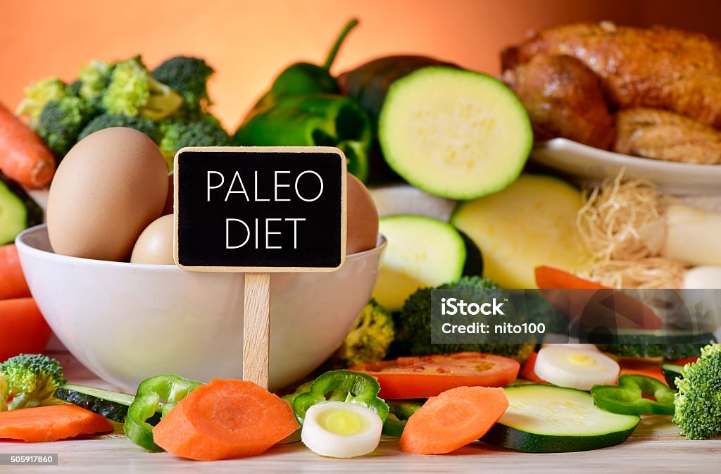 eggs, chicken, vegetables and text paleo diet closeup of a signboard with the text paleo diet on a table full of different raw vegetables, a bowl with some chicken eggs and a chicken Paleo Diet Stock Photo