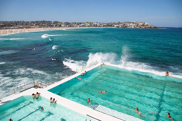 Summer on Bondi Beach, Australia Bondi beach, Sydney, NSW, Australia - November 1, 2015: People swimming in the fresh water swimming pools built in to the sea with waves rolling in to Bondi and breaking against the edge of the pool headland photos stock pictures, royalty-free photos & images