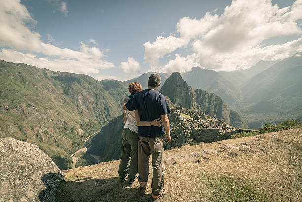 Hugging couple looking at Machu Picchu, Peru, toned image Hugging couple standing in contemplation on the terraces above Machu Picchu, the most visited travel destination in Peru. Rear view, toned, desaturated and vintage styled image. machu picchu photos stock pictures, royalty-free photos & images