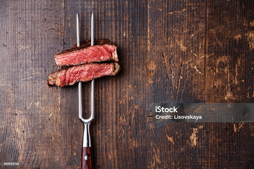 Slices of Steak Ribeye on meat fork Slices of Medium rare grilled Steak Ribeye on meat fork on dark wooden background Meat Stock Photo