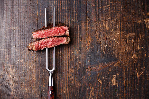 Slices of Steak Ribeye on meat fork Slices of Medium rare grilled Steak Ribeye on meat fork on dark wooden background raw steak beef meat stock pictures, royalty-free photos & images