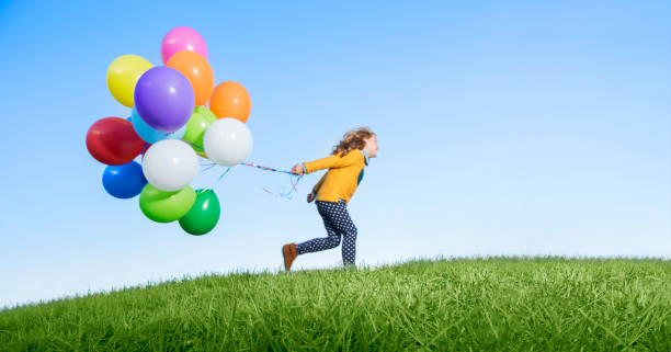 istock Girl playing with balloons on grassy hill 505936623