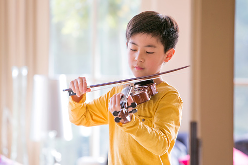 A young boy is playing with a violin, he is concentrating, looking at the instrument.