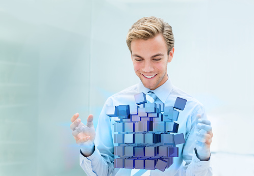 Young business man assembling a floating 3D cube and looking happy - strategy concepts