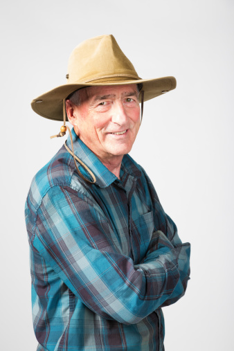 Smiling senior farmer arms crossed, turning. Studio portrait against a gray background.