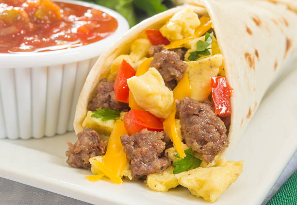 A hot breakfast burrito with egg and sausage close up of a hot fresh breakfast burrito with eggs,sausage,cheese,tomatoes,cilantro, and salsa on the side burrito stock pictures, royalty-free photos & images