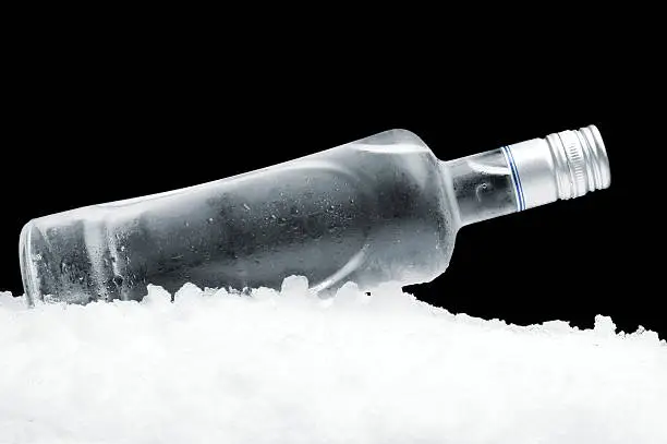 Close-up view of bottle of vodka lying on ice on black