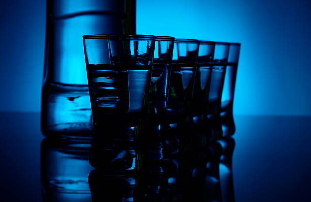 istock Bottle of vodka with many glasses lit with blue backlight 505956813