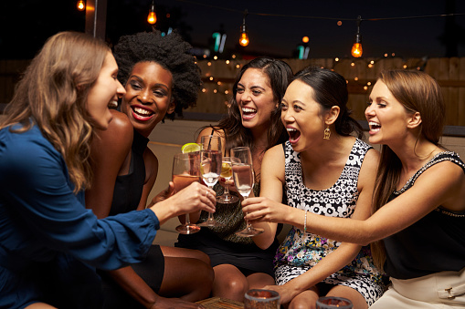 Portrait of happy beautiful teenage girl holding martini glass while sitting with friend at outdoor bar