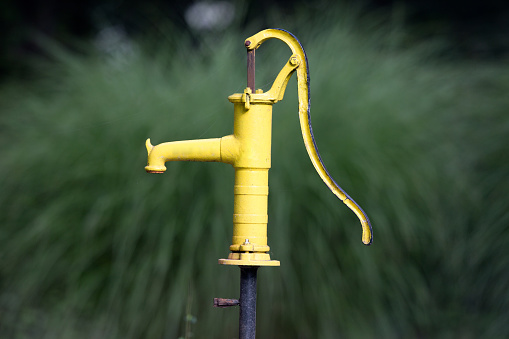 Yellow old water pumping well in courtyard with green background