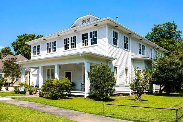 Luxurious single-family homes line a peaceful street in an affluent East Houston in Texas. Trees provide shade over meticulously manicured lawns. Houses showcase a mix of traditional and colonial styles with brick facades, columns, and large windows