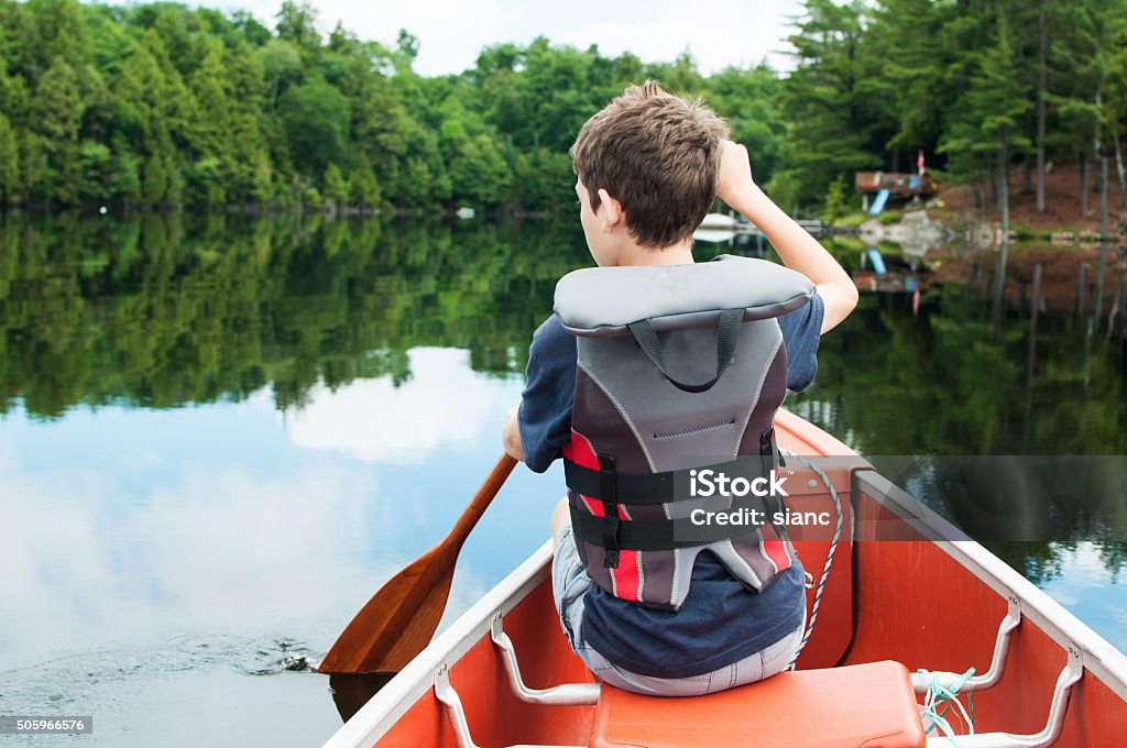 boy in a canoe young boy paddling in a calm lake in the front of a canoe Child Stock Photo