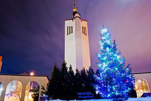 Church bell with new year tree with shining garland at moon light at frozen evening
