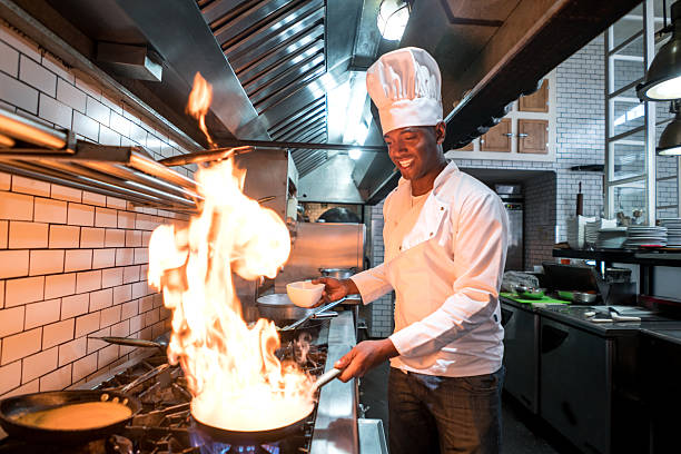 chef flaming nourriture dans un restaurant - chef restaurant cooking african descent photos et images de collection