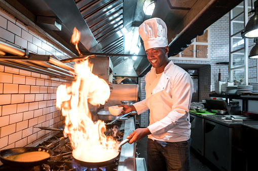 African American chef flaming food and working in the kitchen of a restaurant looking very happy