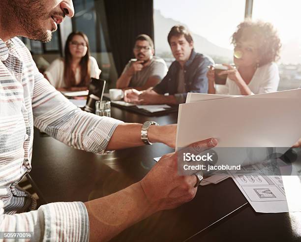 Young Man Explaining Business Plan To Colleagues Stock Photo - Download Image Now - Reading, Research, Report - Document