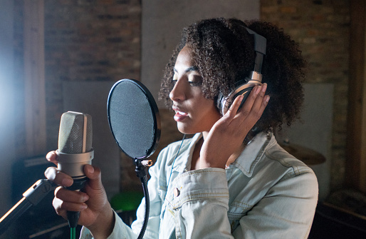 Beautiful African American singer recording in a music studio and wearing headphones