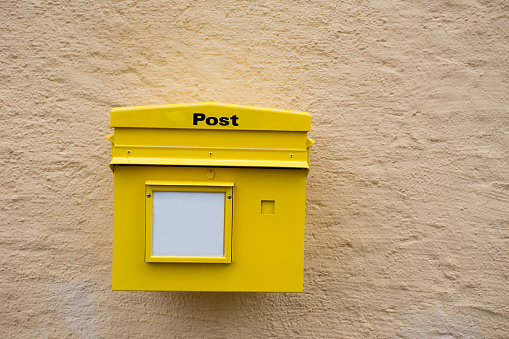 Yellow postbox mounted on wall with whiteboard for text