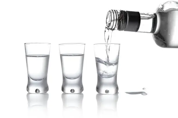 Photo of Bottle and glasses vodka poured into glass isolated on white