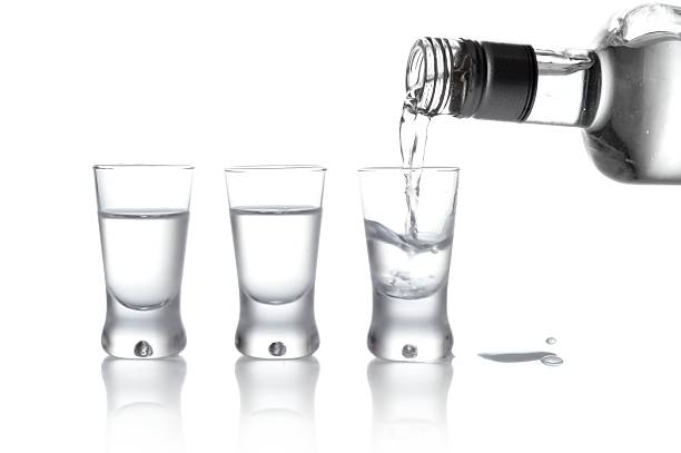 garrafa de vodka e óculos despeje em vidro isolado a branco - shot glass imagens e fotografias de stock