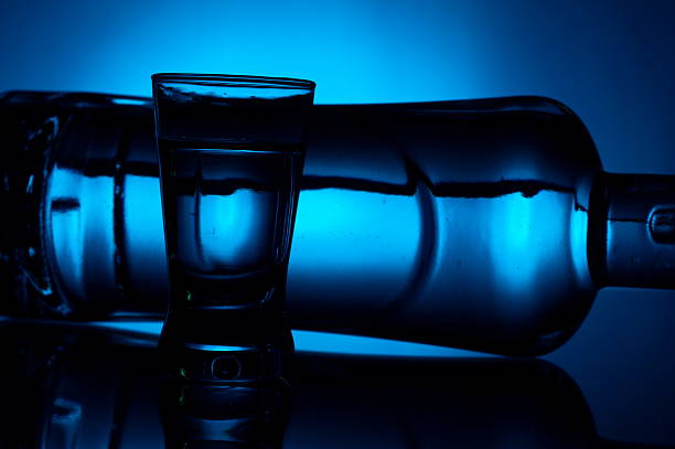 istock Bottle of vodka lying with glass lit with blue backlight 505979357