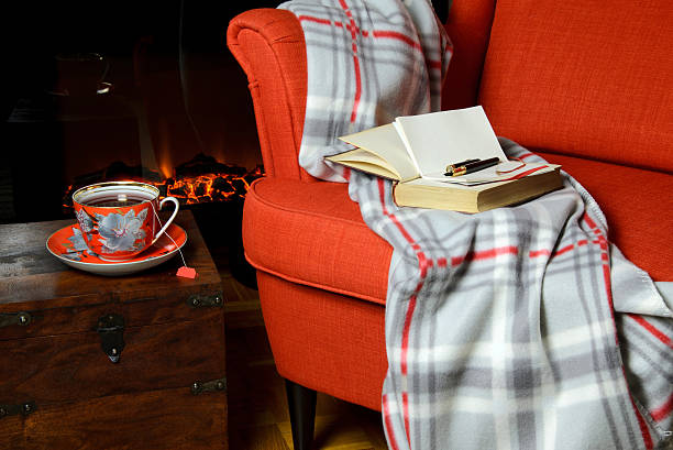 Blanket and tea cup by the fireplace Soft blanket on armchair and a cup of tea by the fireplace fireplace and armchair stock pictures, royalty-free photos & images