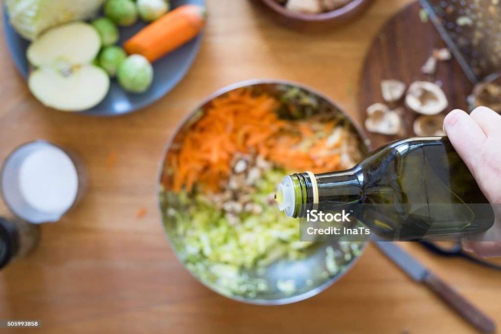 Pouring olive oil from bottle onto salad Pouring olive oil from bottle onto cabbage and carrot salad. Selective focus Cooking Stock Photo