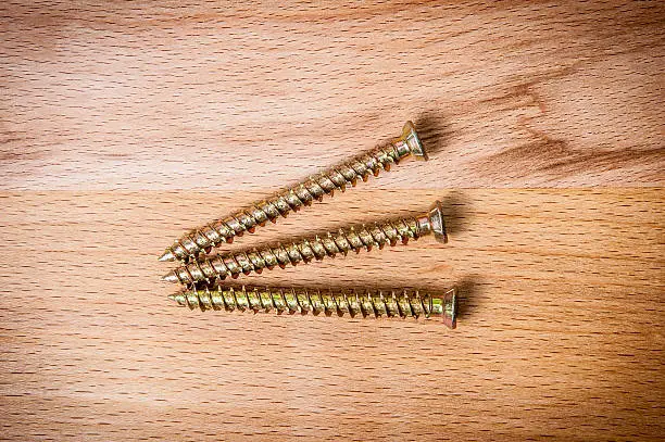 Three goldish screws on wooden background, macro shot