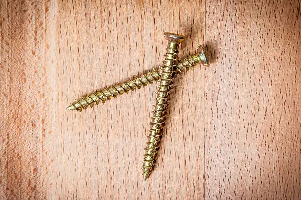 Two goldish screws on wooden background, macro shot