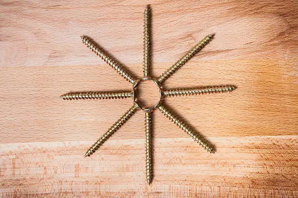 Octactinal star consist of goldish screws on wooden background, macro shot