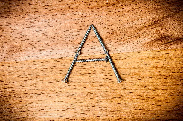 Letter A consist of screws on wooden background, macro shot