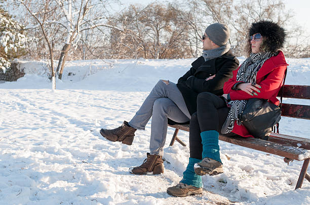 Young couple sitting on bench in park in winter after arguing