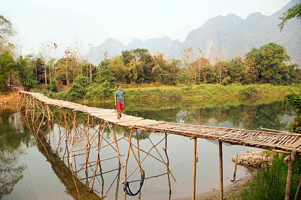 Cheerful Tourist crossing bamboo bridge, limestone view, laos Cheerful Tourist crossing bamboo bridge, limestone view, laos bamboo bridge stock pictures, royalty-free photos & images