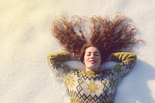 Portrait of a beautiful caucasian girl lying in the snow, enjoying a carefree winter day in the mountains.