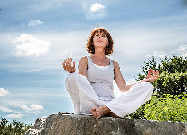 50 de yoga femme en quête de spiritualité sur ciel bleu d'été - senior adult outdoors wellbeing sky photos et images de collection