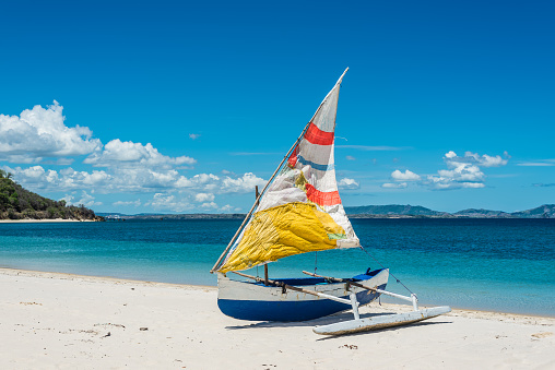 Malagasy outrigger pirogue with colorful makeshift sails on the white beach