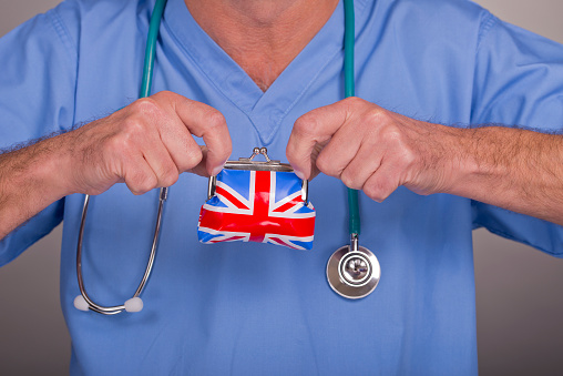 Doctor wearing blue scrubs, with a stethoscope around his neck, holds a Union Jack purse in his hands.