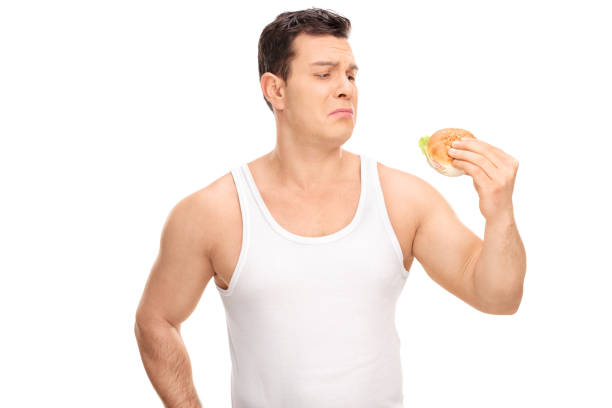 Sad young guy holding a small sandwich Studio shot of a sad young guy holding a small sandwich isolated on white background brat burger stock pictures, royalty-free photos & images