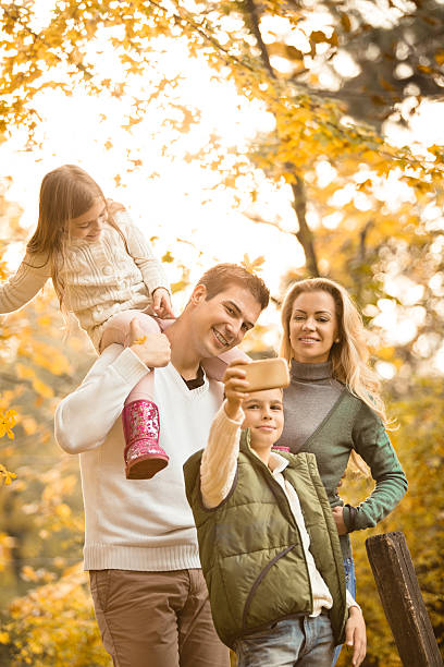 ragazzo a fotografare la sua famiglia in autunno parco - two parent family technology mobility men foto e immagini stock