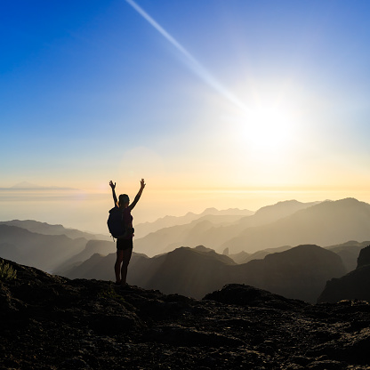 Woman successful hiking climbing silhouette in mountains, motivation and inspiration in beautiful sunset and ocean. Female hiker with arms up outstretched on mountain top looking at beautiful night sunset inspirational landscape.