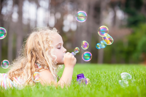 Young girl laying in the grass blowing bubbles.