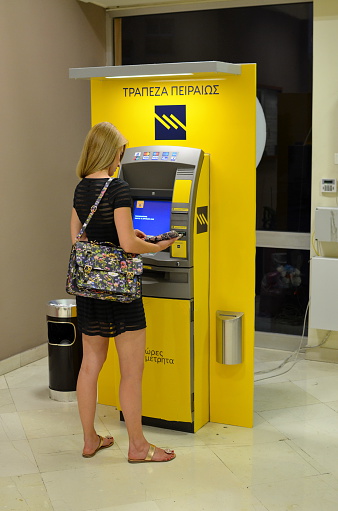 Athens, Greece - July 14, 2015: Greek Woman in front of an (ATM Automated Teller Machine) just before withdrawing some money during the Capital controls in Greece
