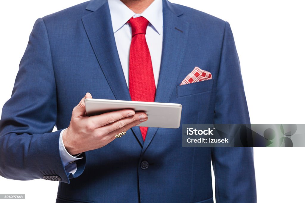 Close up of elegant businessman wearing suit, holding digital tablet Elegant businessman wearing suit, red tie and pocket square, holding a digital tablet. Close up of hand and torso, unregoznizable person. Adult Stock Photo
