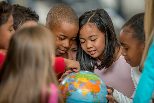 Learning Geography by Looking at the World A multi-ethnic group of elementary age students are learning the places of the world by looking at a globe in geography and history class. elementary student stock pictures, royalty-free photos & images