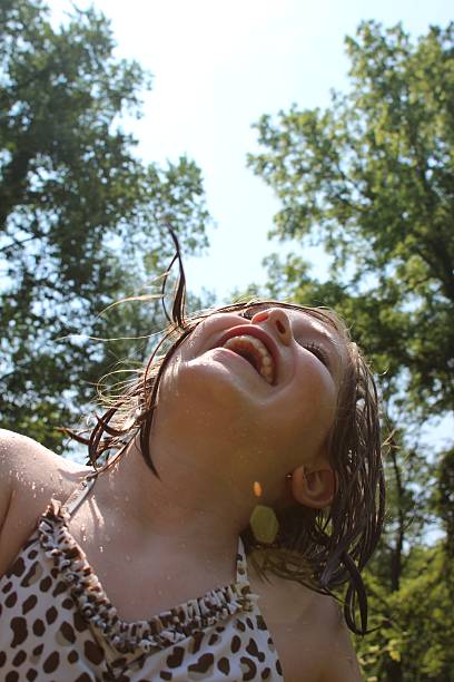 A young girl, 8-10 years old, shakes the water from her hair in the sun