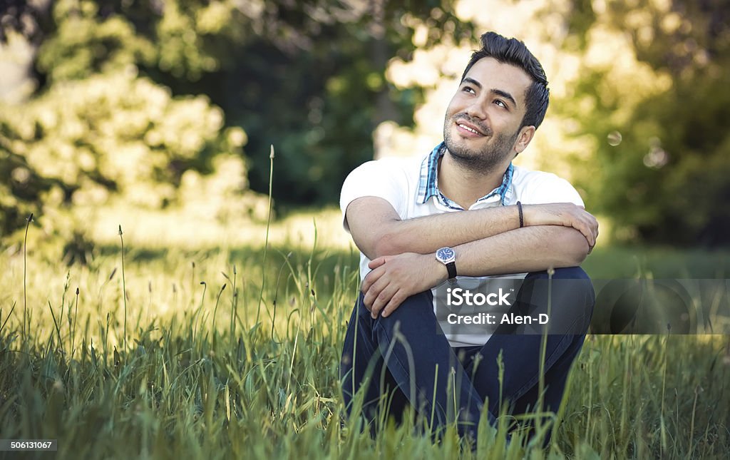 Happy young man sitting on meadow Happy young man sitting on meadow. Gorgeous guy relaxing on grass. Outdoor, daylight Latin American and Hispanic Ethnicity Stock Photo