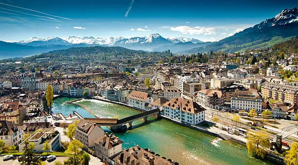 Overview of Lucerne, Switzerland, in a sunny day during springtime. The snow covered mountain range composes the background with a blue sky that shows jet plane traces.